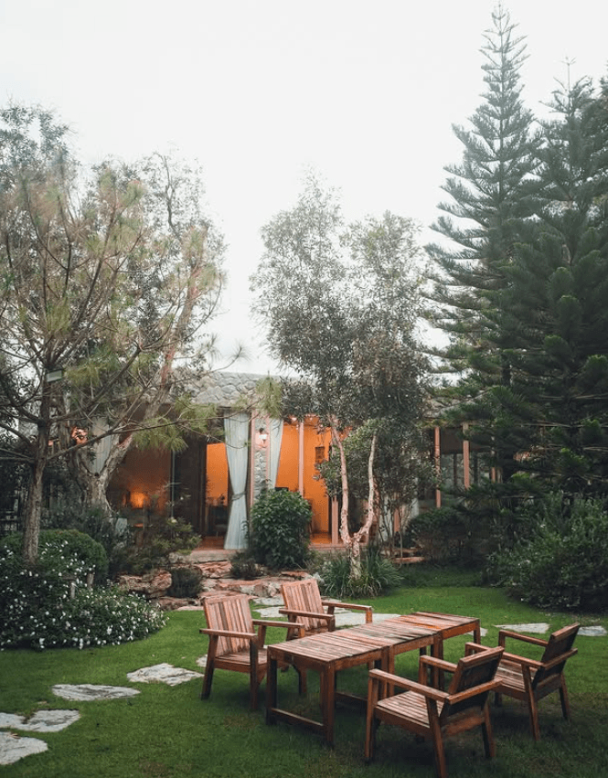 Wooden dining set under olive trees in front of stone villa at dusk