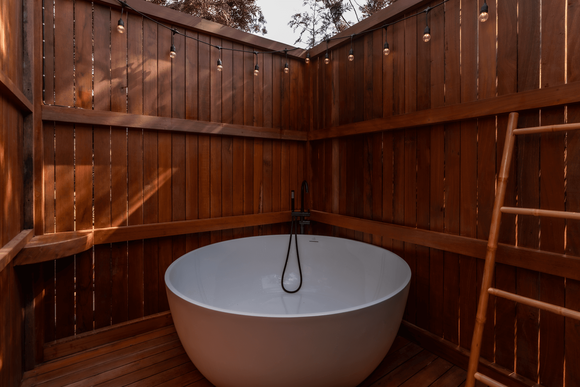Outdoor wooden bath with string lights overhead