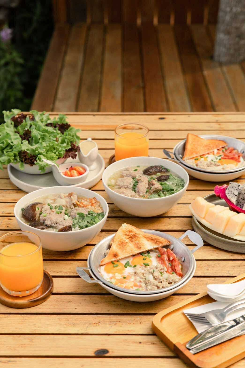 Full Thai breakfast spread — rice soup, skillet eggs, juice and fruits