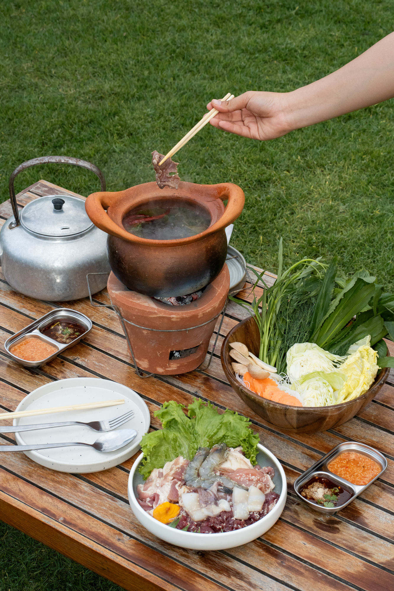 Moo krata outdoor setup with vegetables and dipping sauces